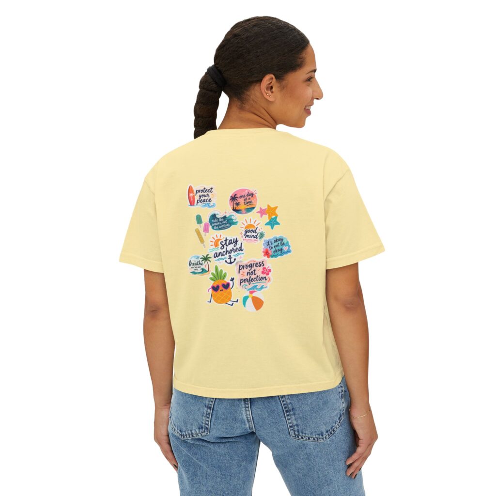 Back view of a person wearing a pale yellow T-shirt with colorful sticker-style graphics on the back, paired with blue jeans.